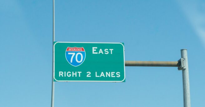 Overhead brightly colored steel highway sign for interstate 70 east right two lanes of high way exit ahead.