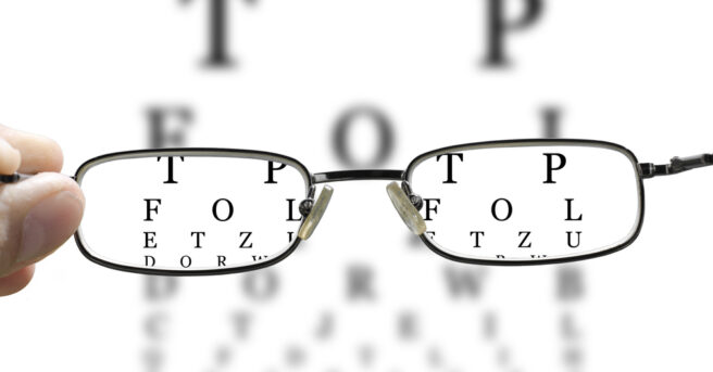 out of focus eye test and a hand holding glasses correcting the vision horizontal
