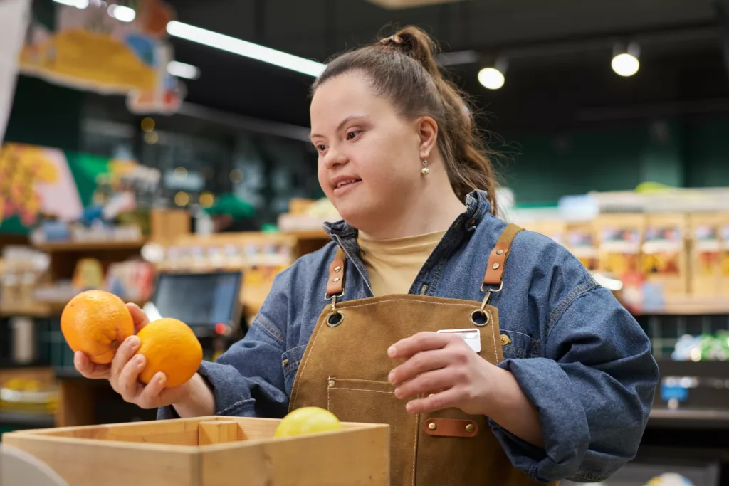 Waist up portrait of smiling young woman with disability working in supermarket sorting fresh fruits and produce