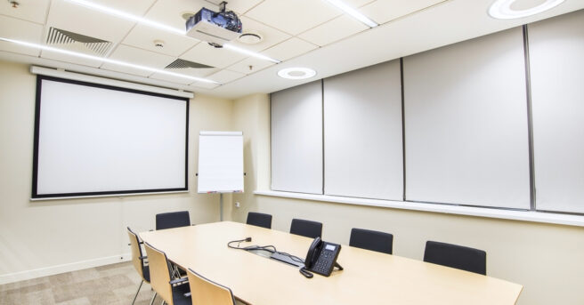 Small empty conference room with TV projector, conference table and chairs.