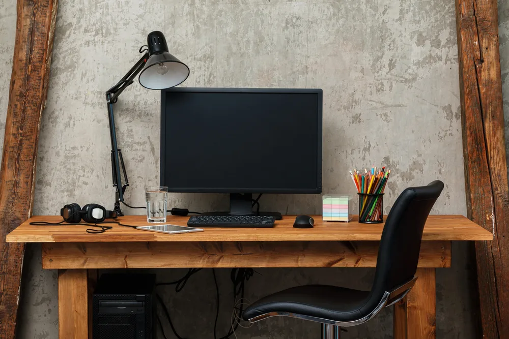 Home office with task lighting and light colored walls, medium colored desk, and a black chair and computer