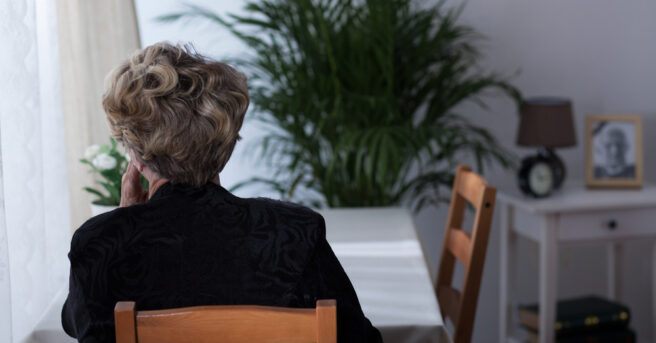 Older person sits alone at a table with their back against the camera