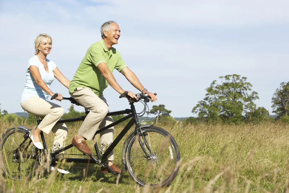 Mature couple riding through grass on a tandem bicycle