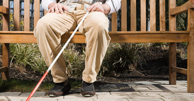 Person sitting on bench holding a white cane