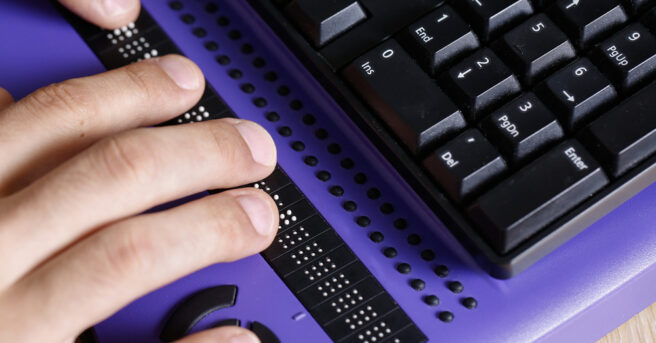 Blind person using computer with braille computer display and a computer keyboard.