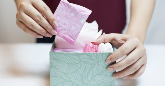 Close up photo of teenage girl picking sanitary pad out of a green box.