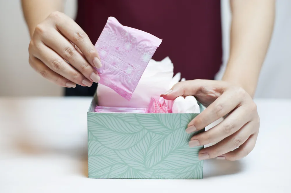 Close up photo of teenage girl picking sanitary pad out of a green box.