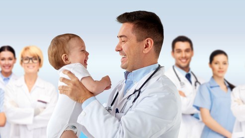 A happy pediatrician holding a baby with other medical professionals standing behind.
