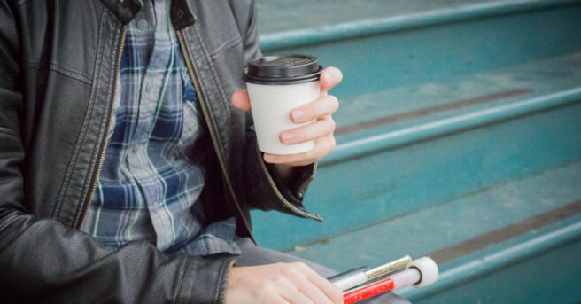Man sits on steps drinking coffee and holding a white cane