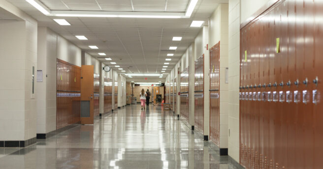 School hallway with lockers with students at the end of the hallway.