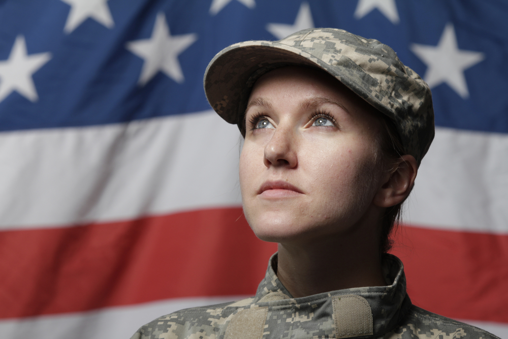 Uniformed soldier stands in front of an American flag