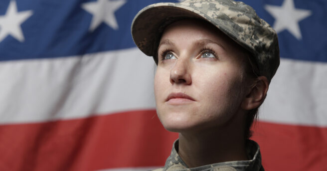 Uniformed soldier stands in front of American flag