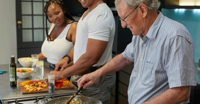Older person sautéing vegetables alongside younger people in a home