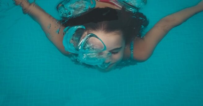 young girl swimming under water releasing air bubbles