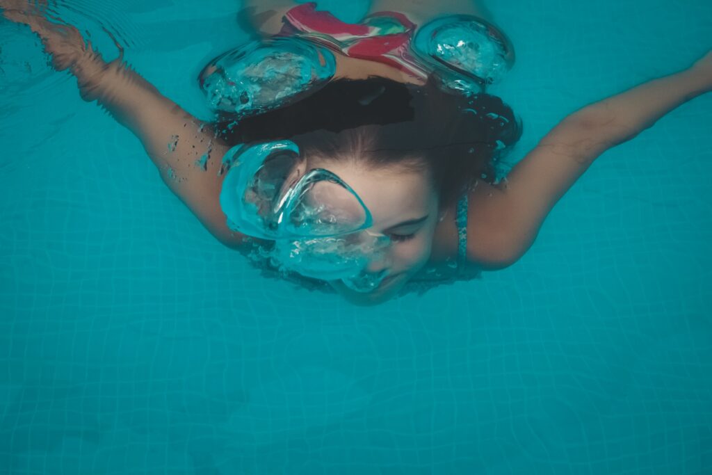 young girl swimming under water releasing air bubbles