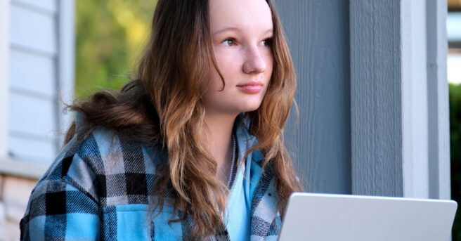 A teen sitting on the porch thinking with a laptop.