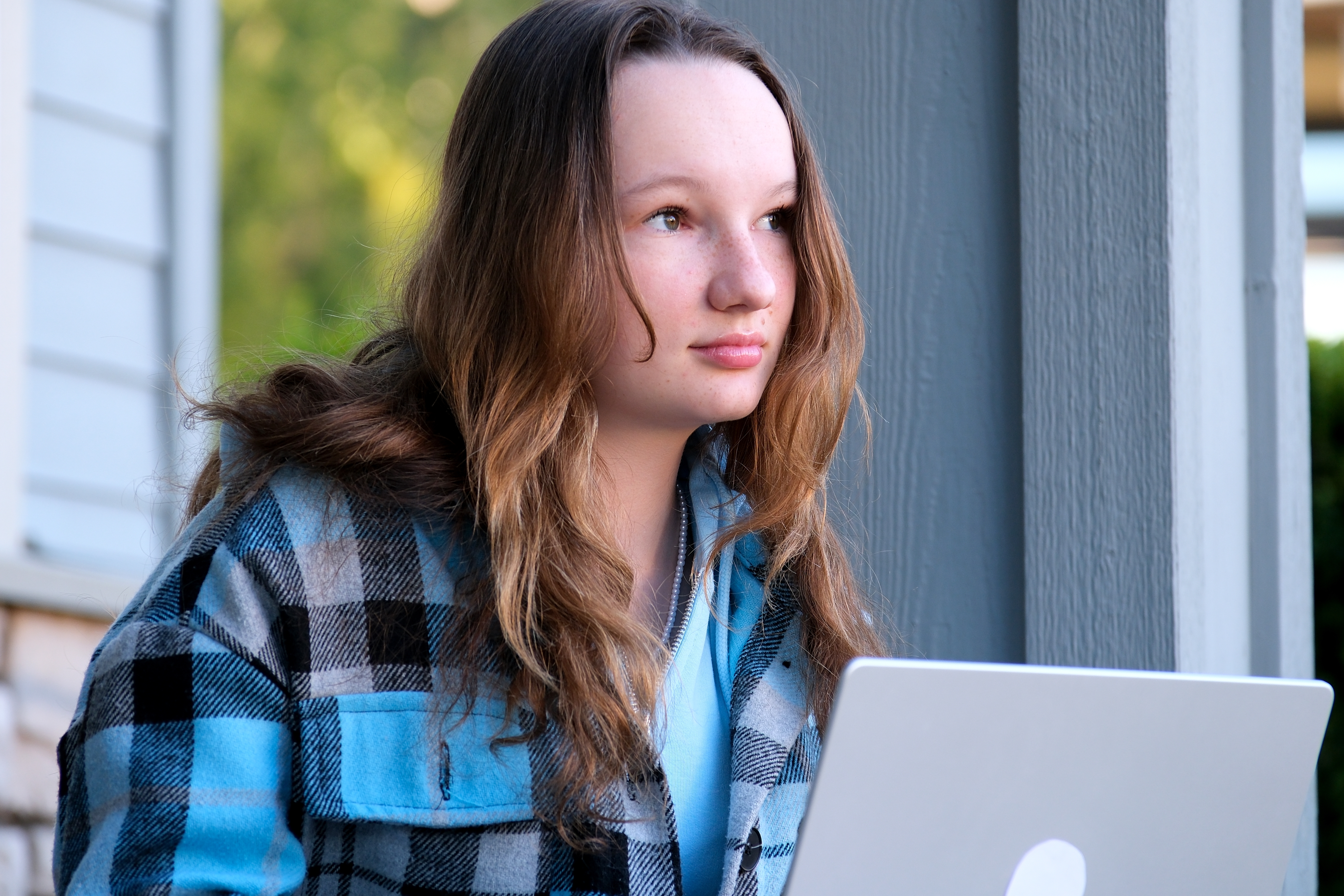 A teen sitting on the porch thinking with a laptop.