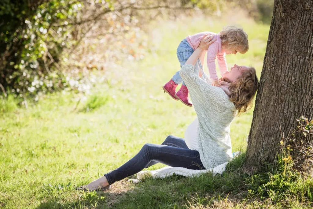 a mother sitting under a tree holding her child up in the air