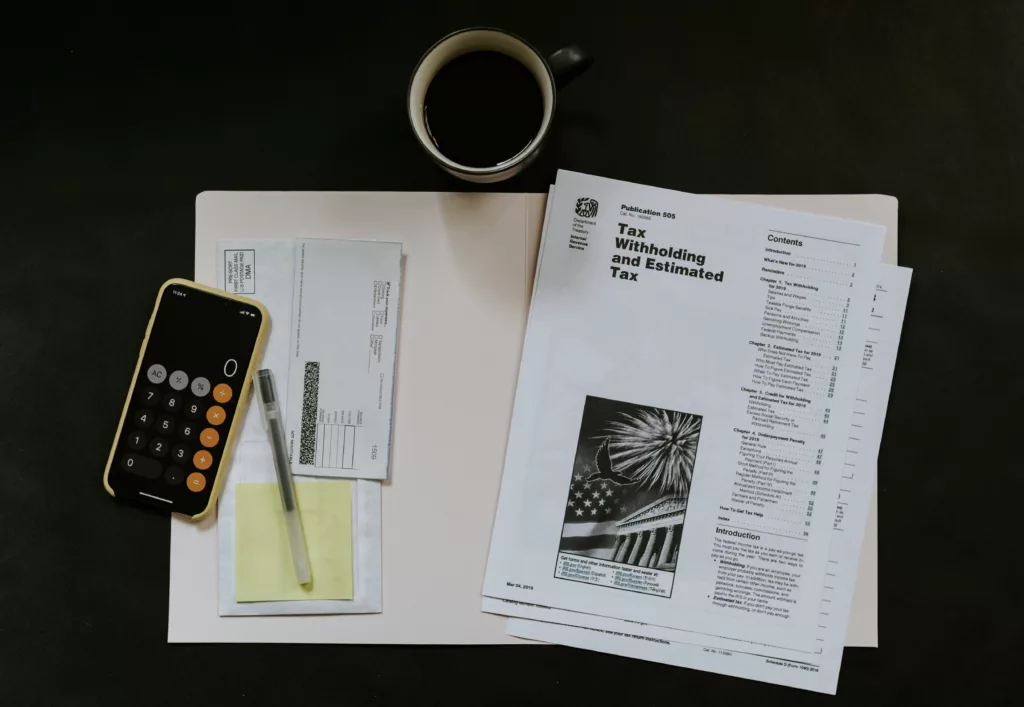  tax documents rest on a table with an iPhone calculator, check, pen, and cup of coffee