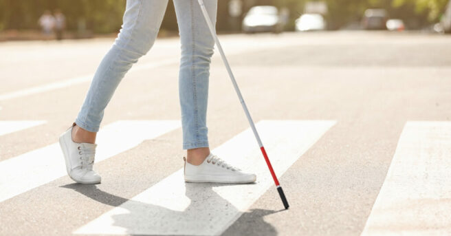 individual walking across a cross-walk with an extended white cane