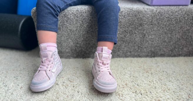A toddler feet in pink shoes on the ground as they are sitting on a step.