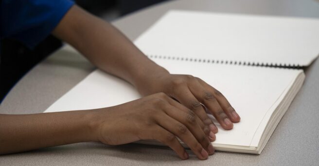 Photo of child's hands reading braille page from book.